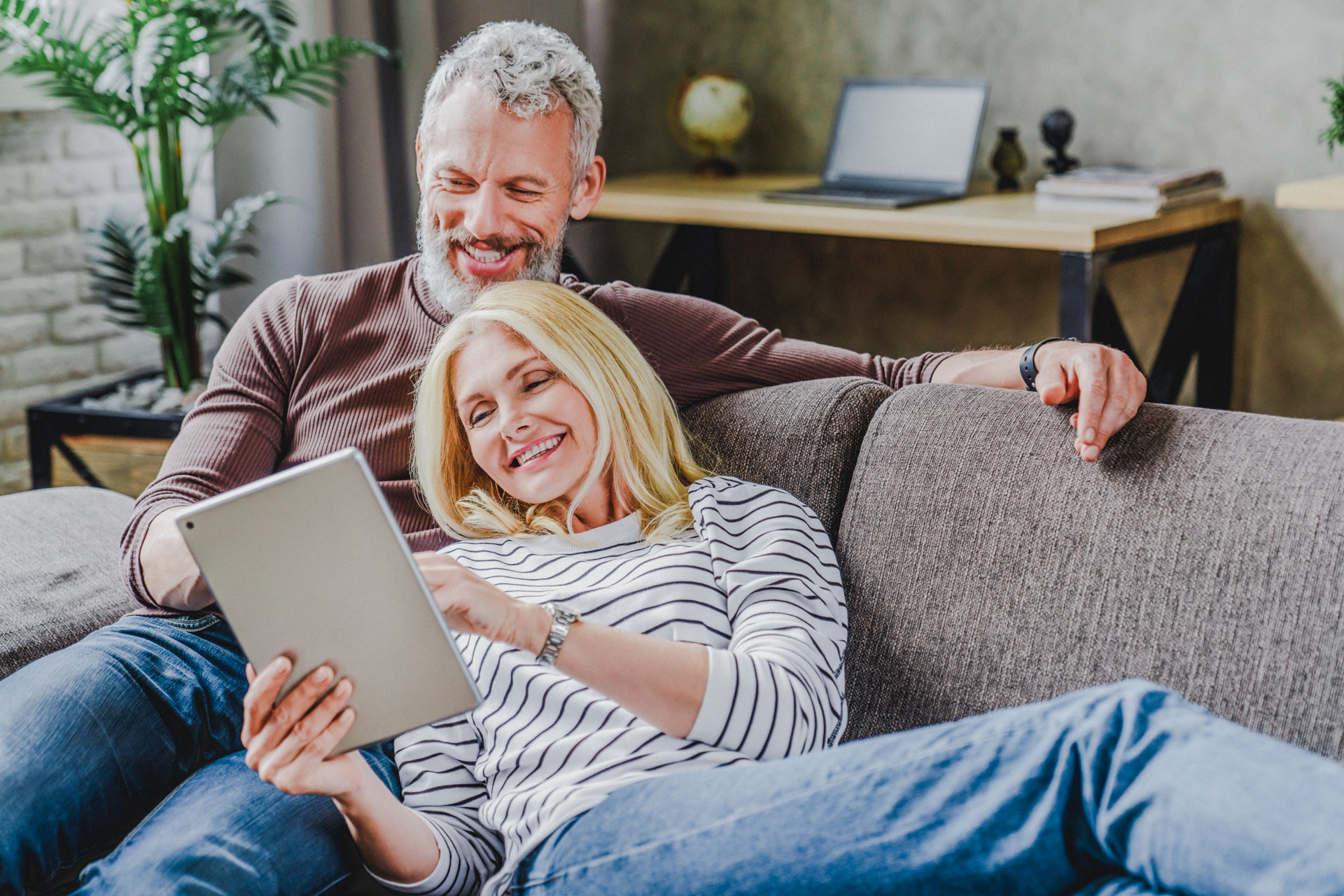 Happy senior couple using digital tablet on sofa indoors